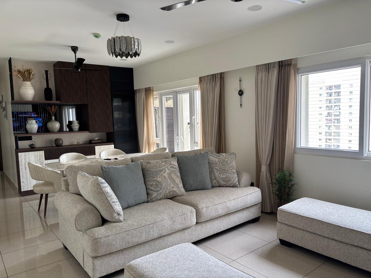 Open-plan living and dining space with a beige upholstered sofa and paisley cushions, a feather-shade pendant light, floor-length curtains