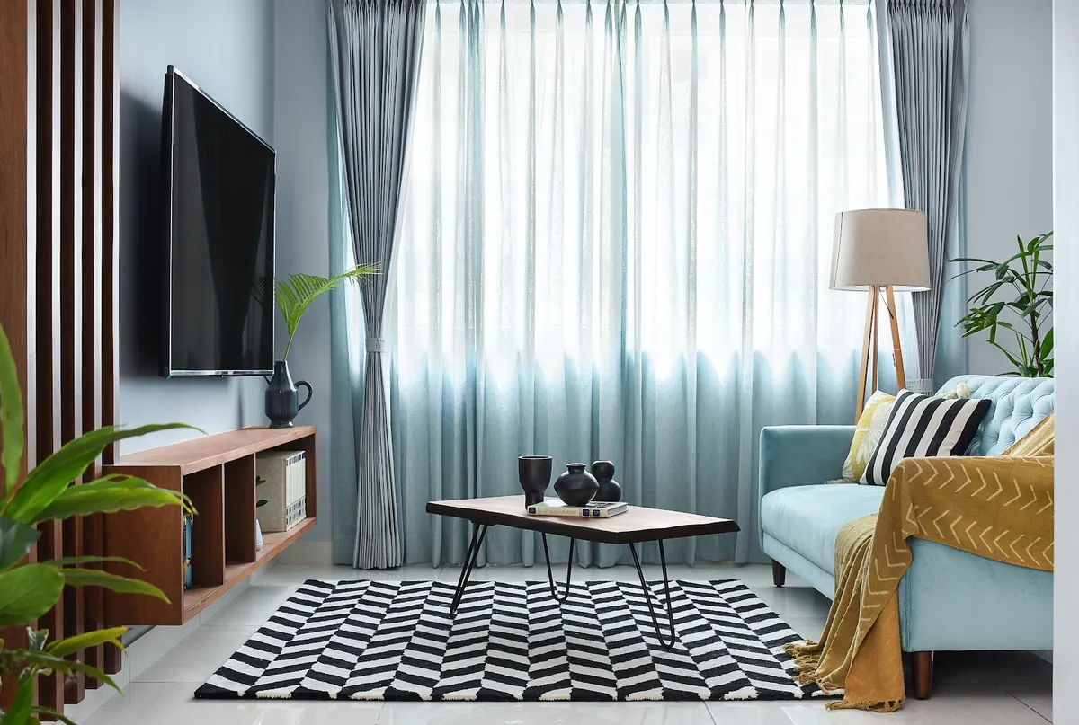 Living room with a teal tufted sofa, a black-and-white chevron rug, a hairpin-leg wood coffee table, and ombre sheer curtains.