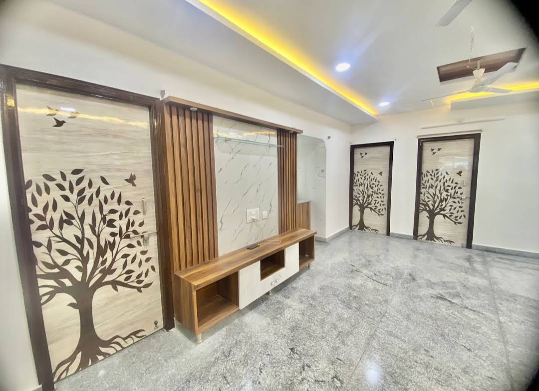 Living area with a wood-and-white TV console beneath a yellow cove-lit ceiling, flanked by internal doors printed with a tree-silhouette motif.