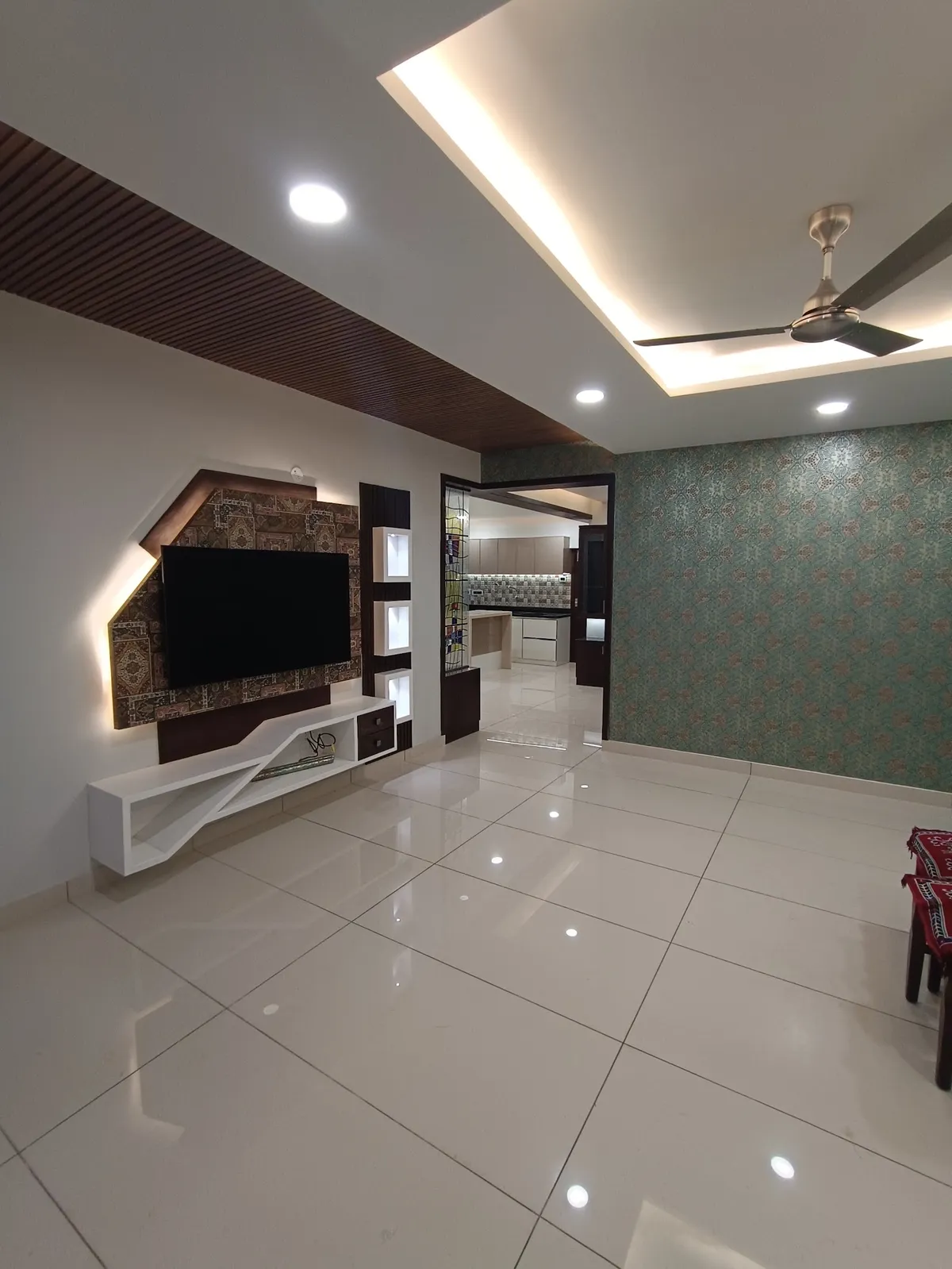Real photo of a living room with an angular floating TV console below a backlit patterned wall panel, a teal damask-print wallpaper accent wall