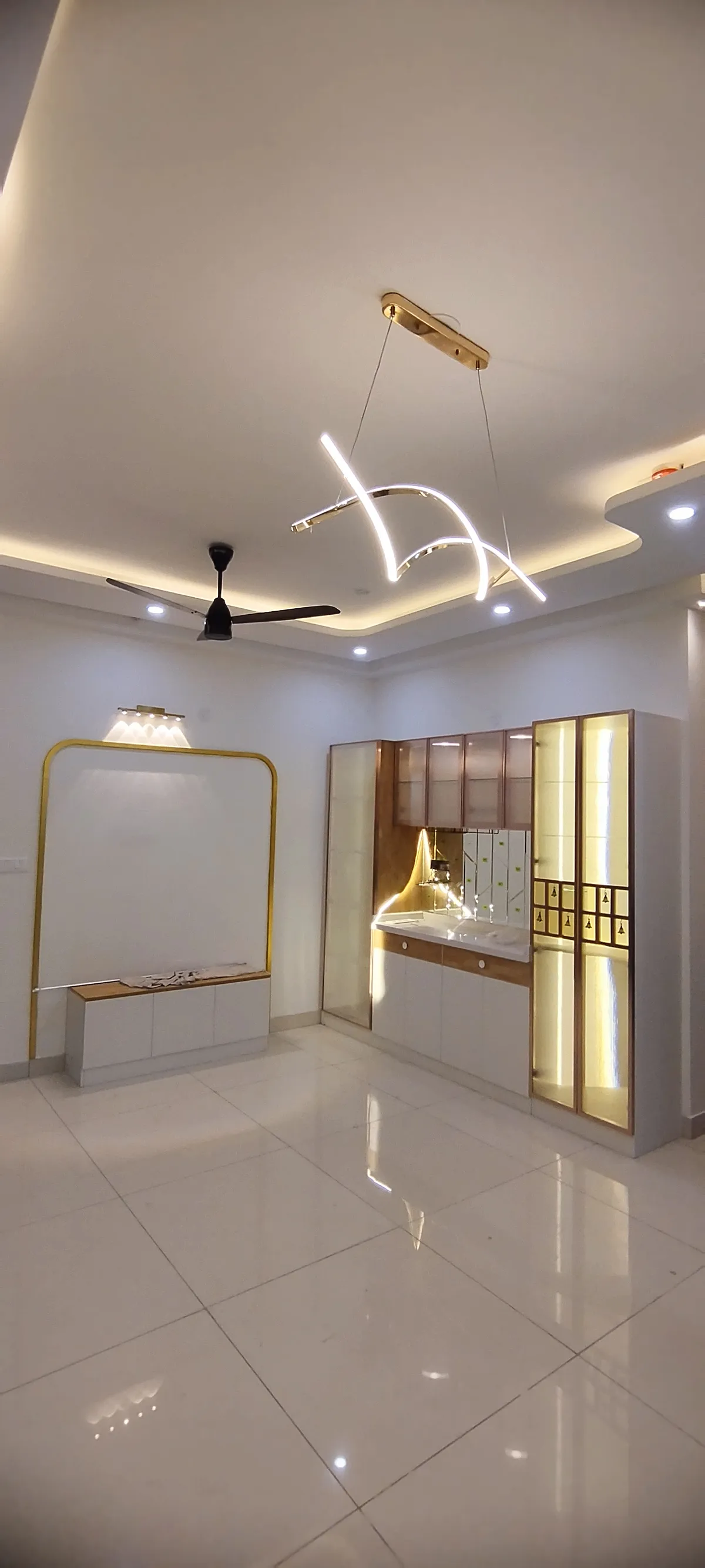 Foyer with a backlit glass-door pooja unit featuring a laser-cut bell motif panel, a sculptural arc pendant light