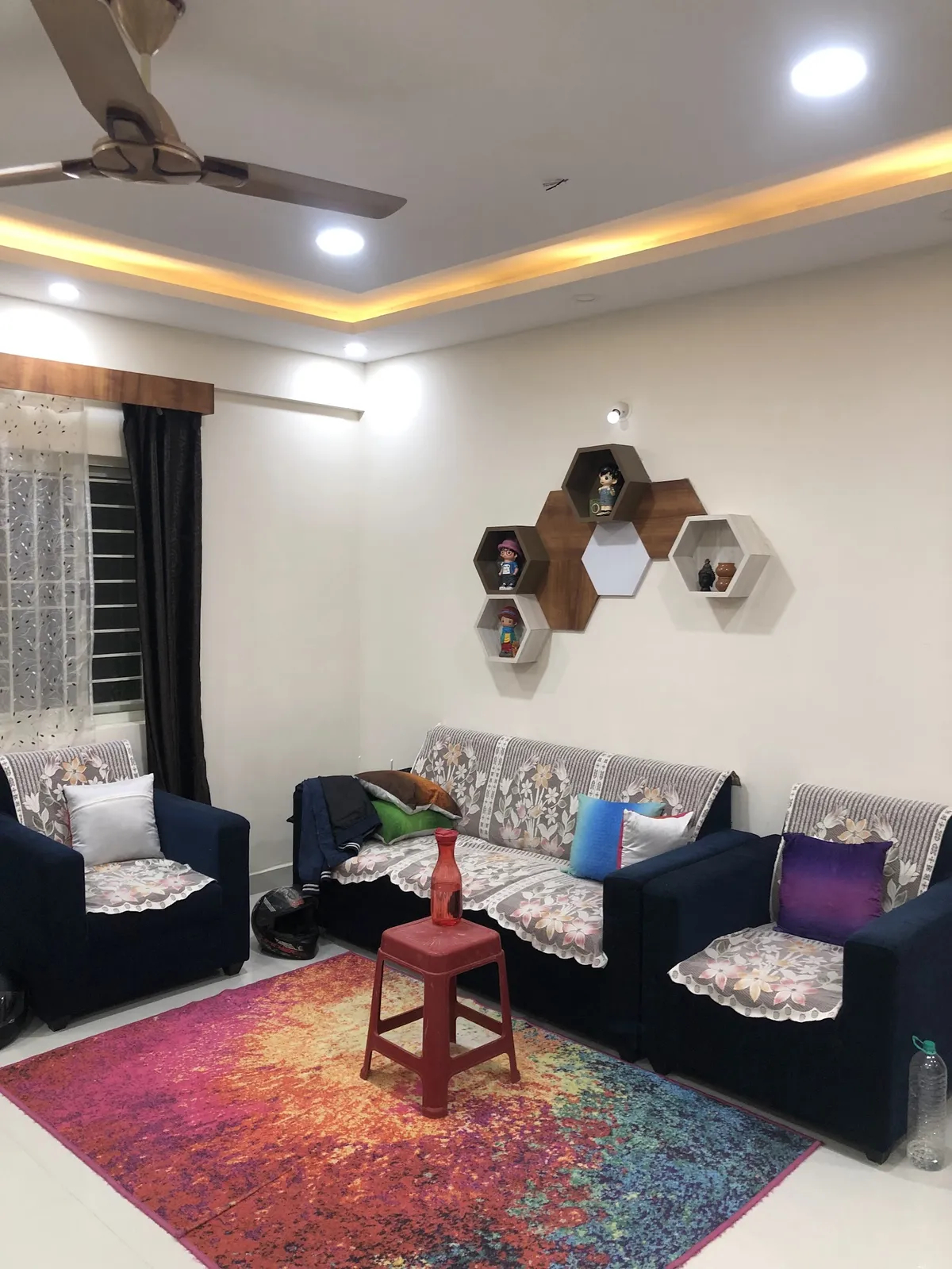 Living room with navy sofas dressed in floral lace covers, a colourful gradient rug, and a hexagonal honeycomb display shelf styled with figurines