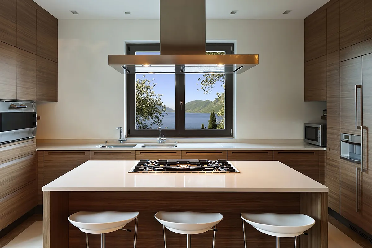 Walnut-veneer kitchen wrapped around a central island with a five-burner hob and a bronze-trim island hood