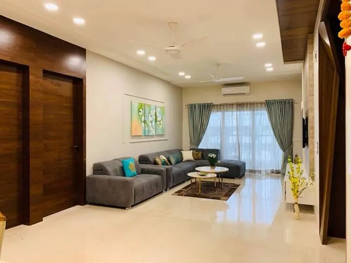 Living room with a grey L-sofa and teal cushions set against a full-height teak veneer wall of flush concealed doors, a floral diptych alongside