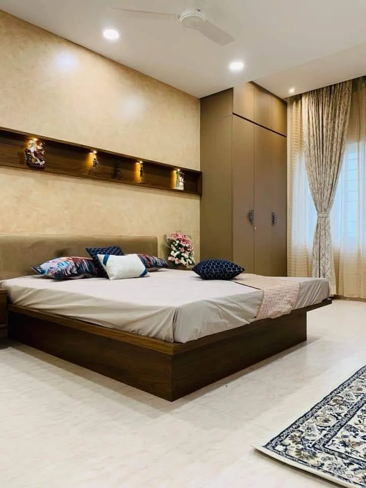 Master bedroom with a floating wood-platform bed and upholstered headboard, a textured wall with a lit display niche for idol figurines, a wardrobe