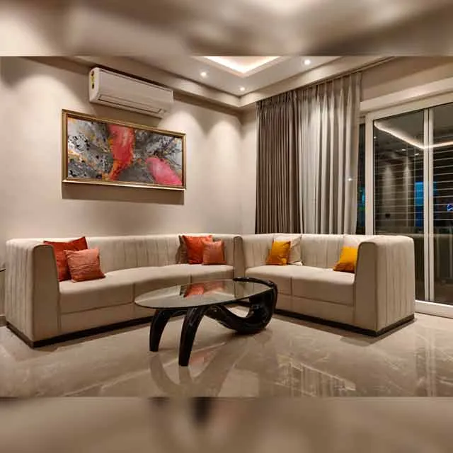 Real L-shaped living room with a channel-tufted cream sectional sofa, coral and mustard accent cushions, a sculptural black coffee table