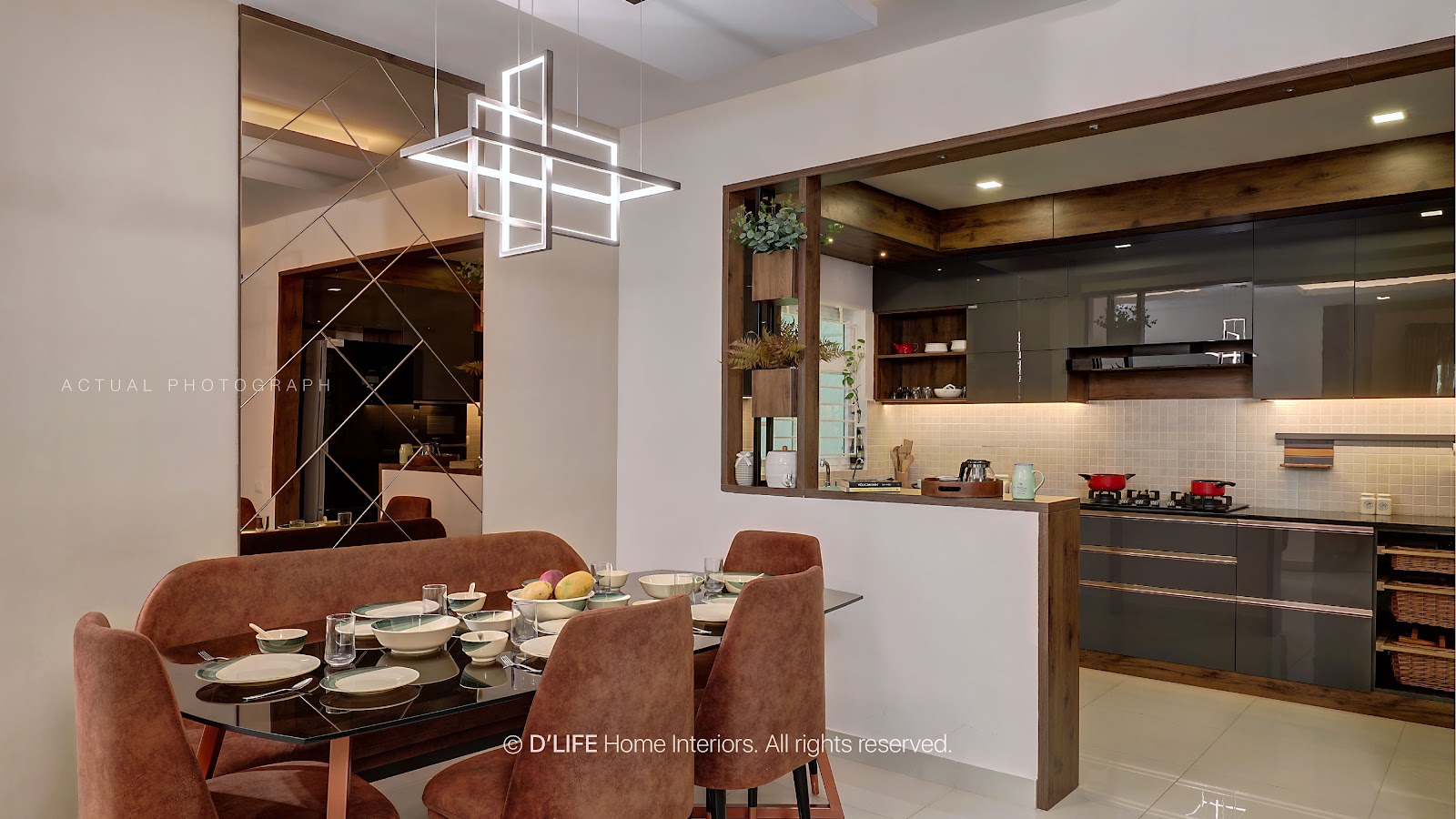 Dining area with a glass-top table and terracotta velvet chairs under a geometric cube pendant light, a diagonal-cut mirror wall