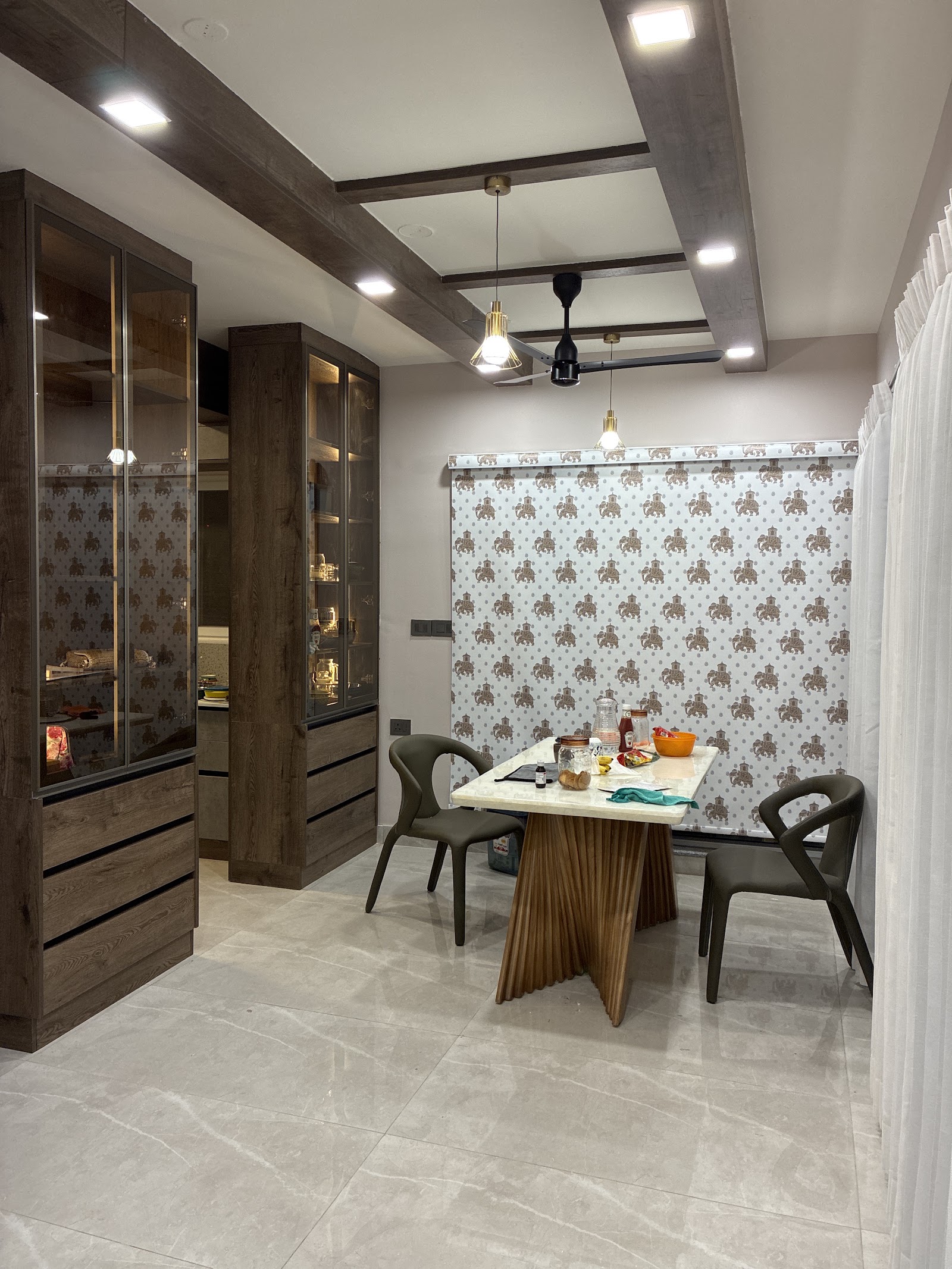 Dining nook with elephant-motif wallpaper backdrop, a sculptural pleated-wood-base marble dining table, olive bucket chairs