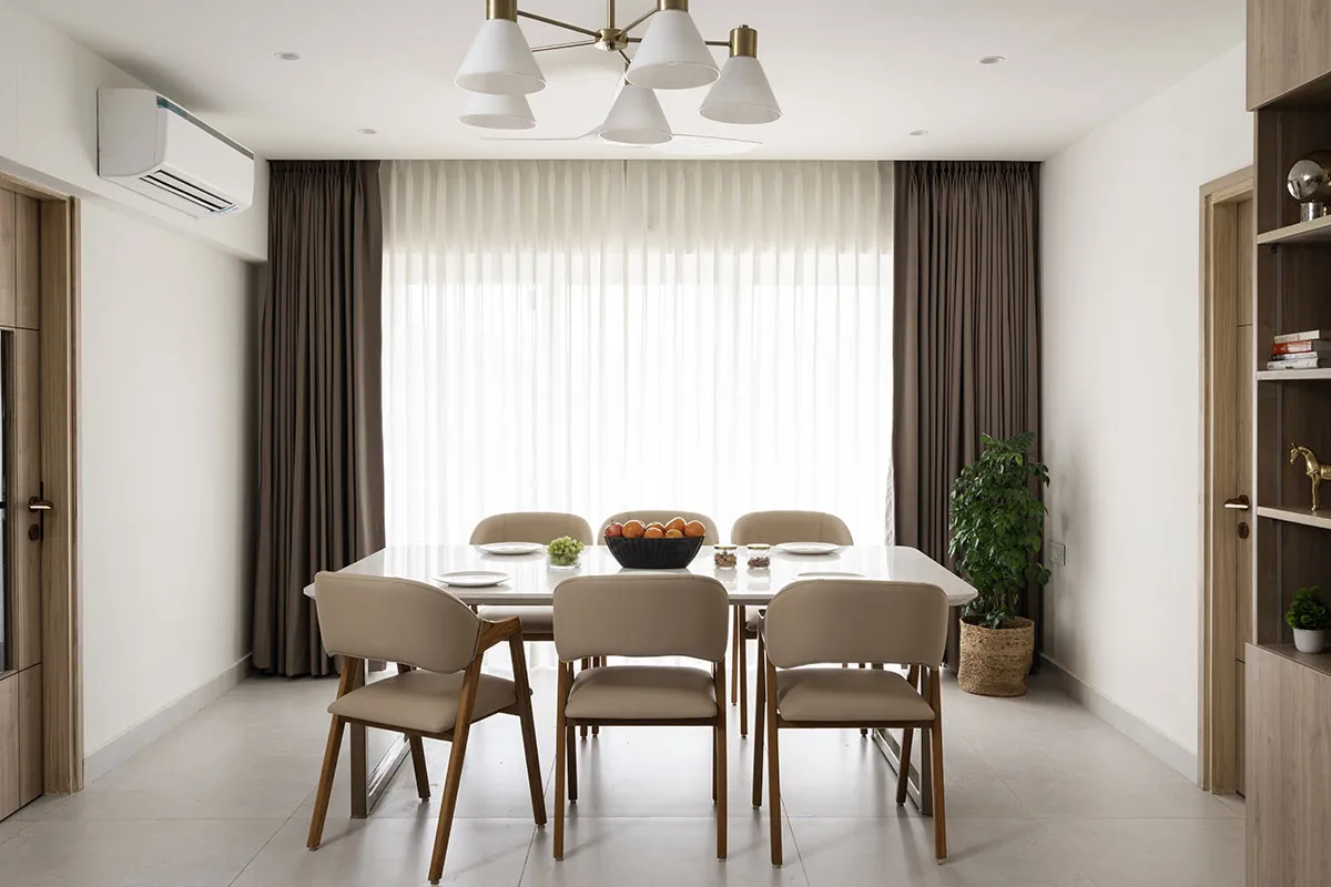 Six-seater dining room shot straight into a blown-out sheer-curtained window, taupe leather-look chairs on splayed wood legs and a six-arm brass-and-white cone