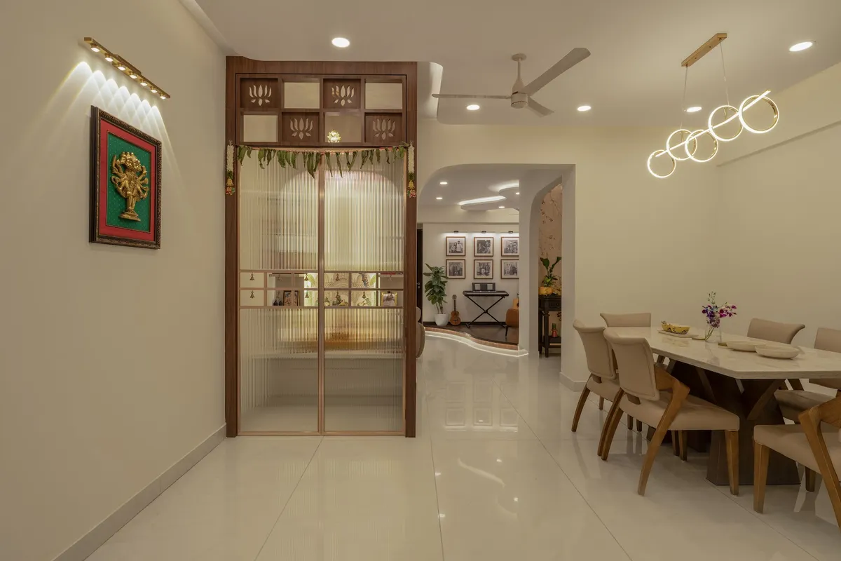 Fluted-glass pooja enclosure with a lotus-jaali top panel and a fresh mango-leaf toran, framed in walnut