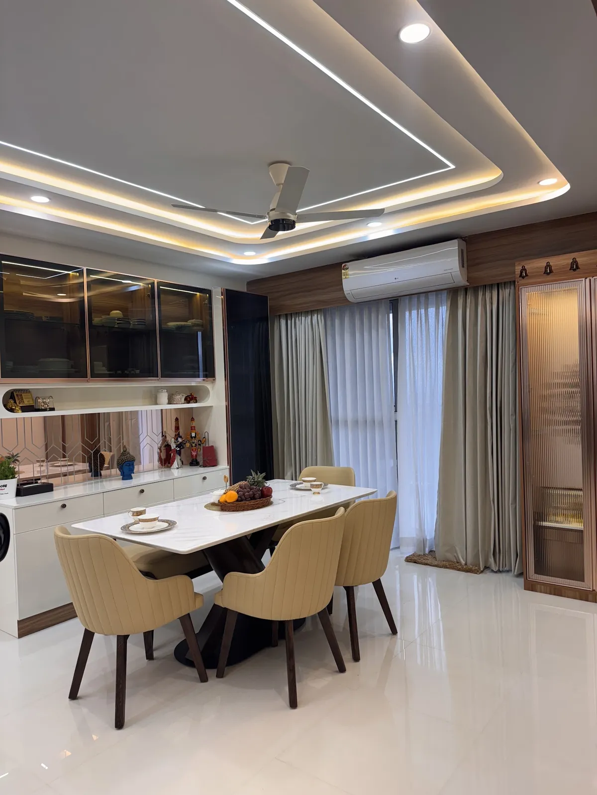 Six beige channel-stitched chairs round a white sintered-stone dining table, with a rose-gold framed smoked-glass crockery unit over a mirrored curio niche