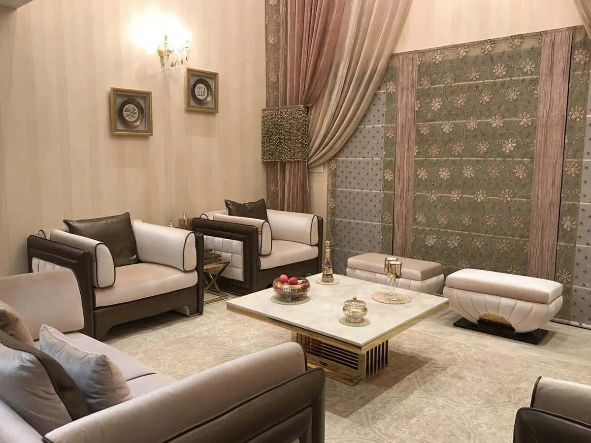 Majlis-style living room with dark-trimmed cream leather armchairs, a marble-and-gold coffee table, a richly patterned floral tapestry wall panel