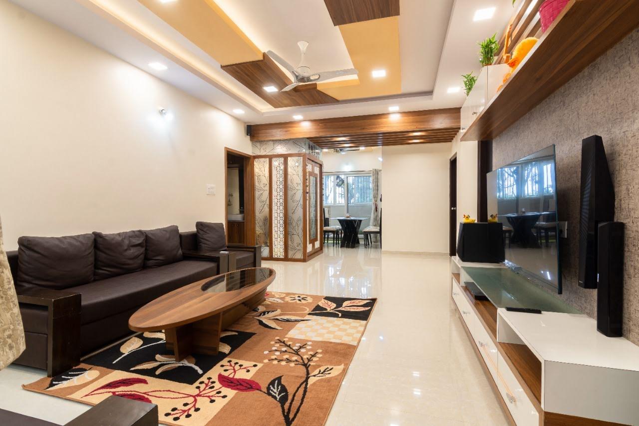 Real photo of an open living-dining apartment with a stepped wood-and-POP false ceiling, a jaali-screened pooja nook off the hallway