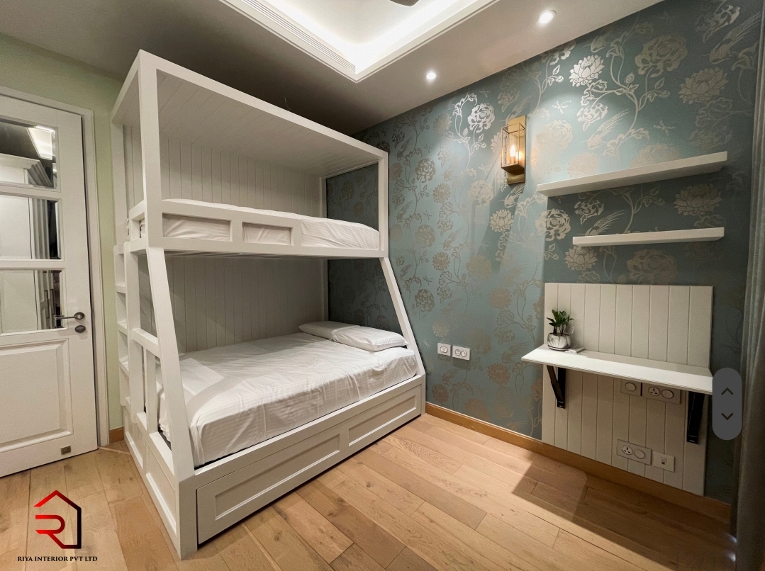 Kids' bedroom with a white built-in bunk bed with trundle drawer, blue floral wallpaper accent wall, and a floating study shelf with wall sconce.