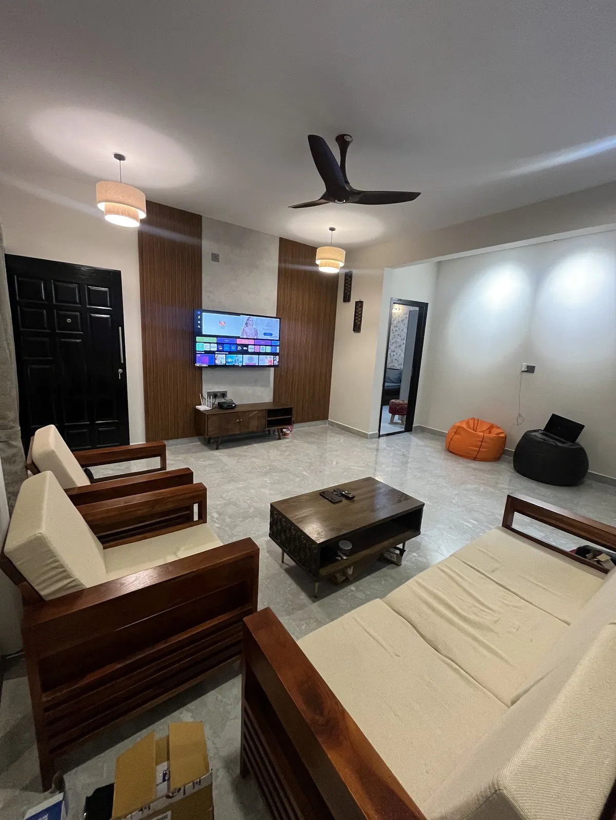 Living room with a wood-frame sofa set in cream upholstery, a wood-panelled TV wall with a floating console