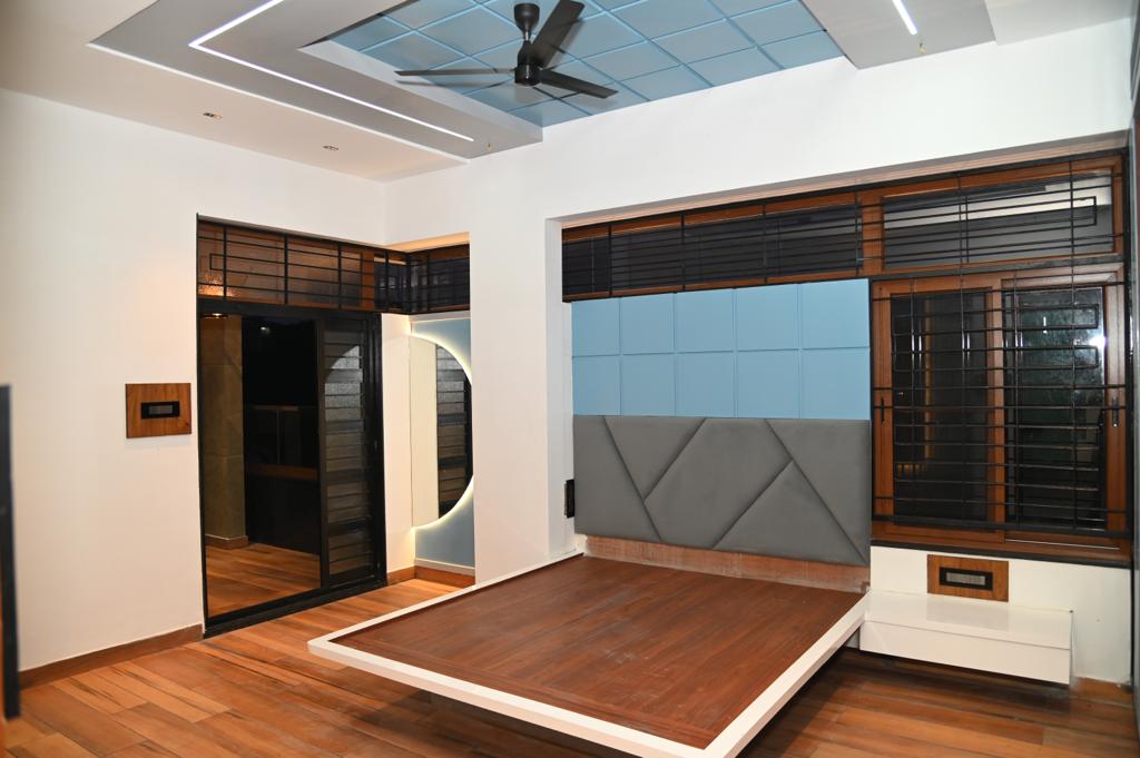Bedroom with a raised wood platform bed frame, a grey-and-blue geometric quilted headboard wall, and a checkered blue false-ceiling panel above.