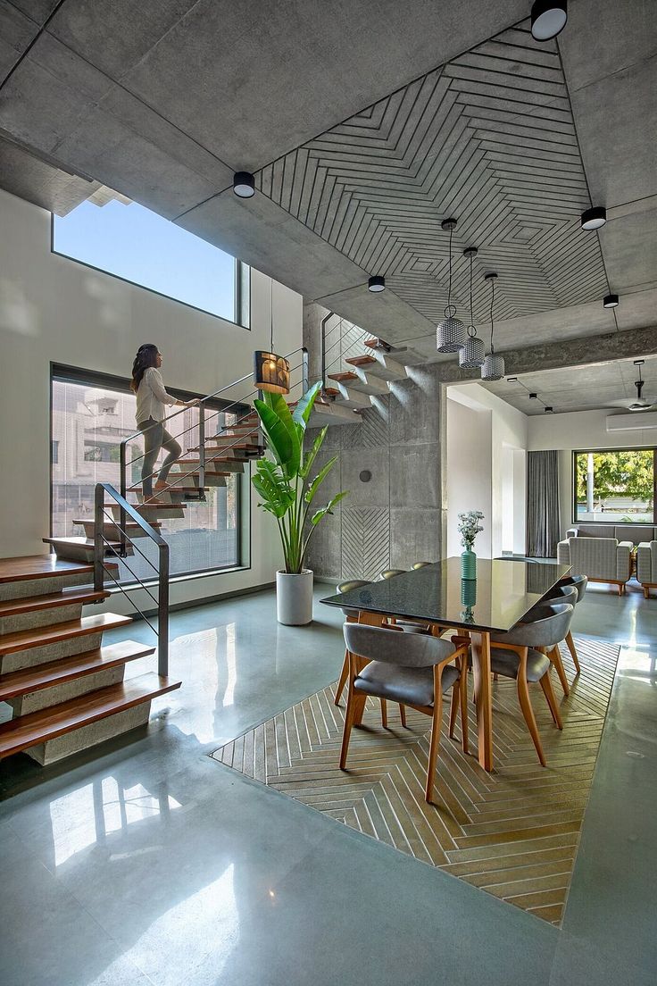 Double-height dining space with a floating wood-and-steel staircase, a chevron wood-panelled concrete ceiling