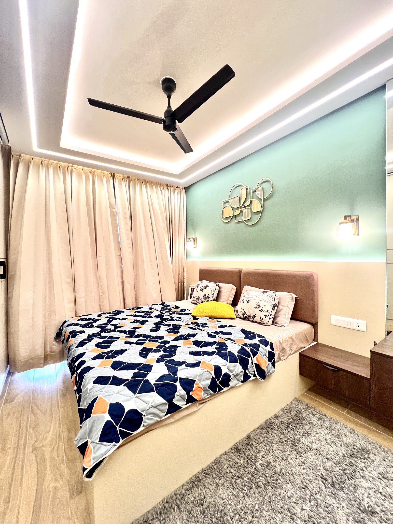 Real bedroom photo with a mint-green cove-lit accent wall behind a blush upholstered headboard, a floating bedside console