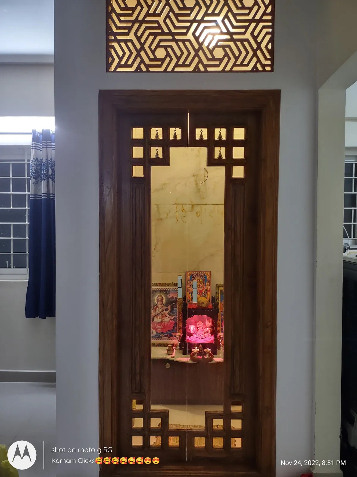A traditional wooden pooja room with a carved jaali door fitted with brass bells, a geometric jaali transom