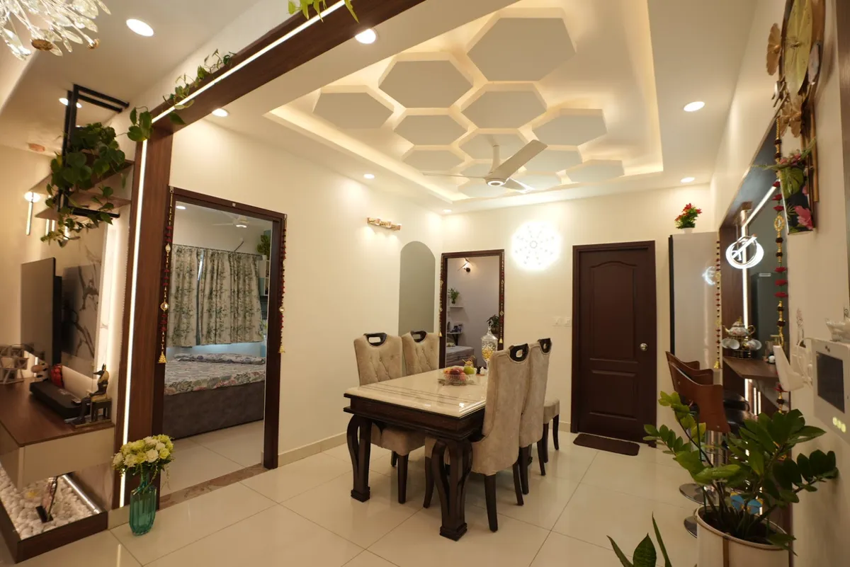Dining area under a honeycomb-coffered POP ceiling with cove lighting, a marble-top six-seater on carved dark-wood legs with cream upholstered chairs