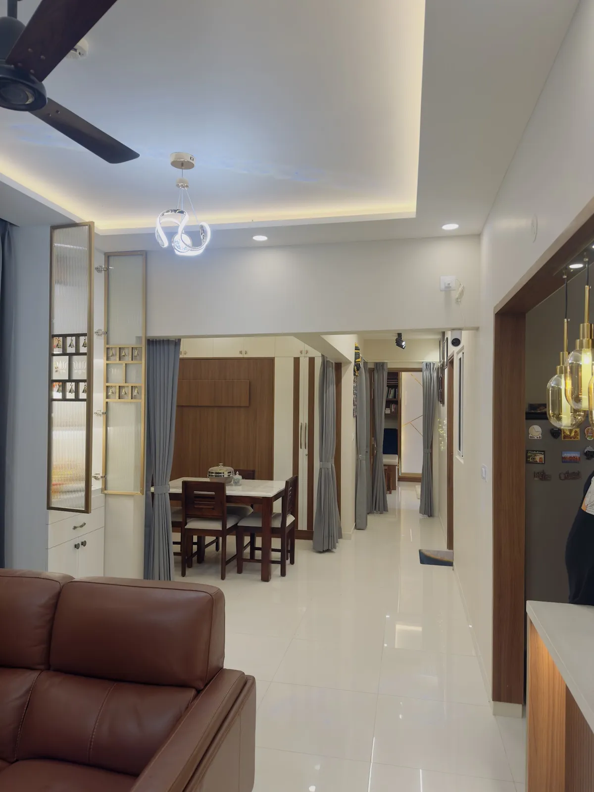A wide open-plan view from a brown leather sofa through a dining table set to a hallway leading to a bedroom