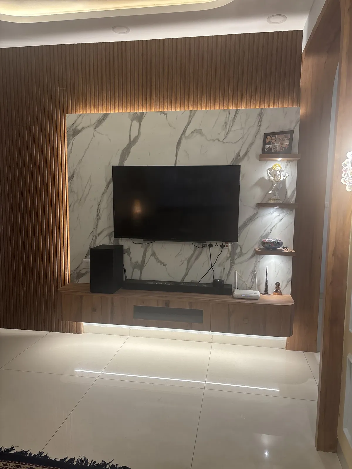 TV wall framed by vertical walnut fluted panelling around a statuario-look slab, with a wall-hung console lit by an under-strip and three floating shelves