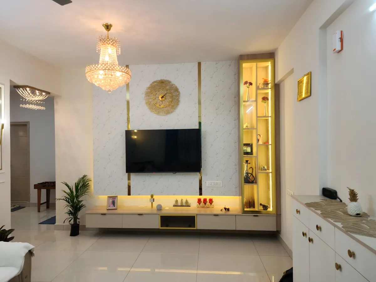 Living room TV wall in patterned off-white wallpaper edged with gold strips, a gold sunburst clock above the screen and a backlit gold display column