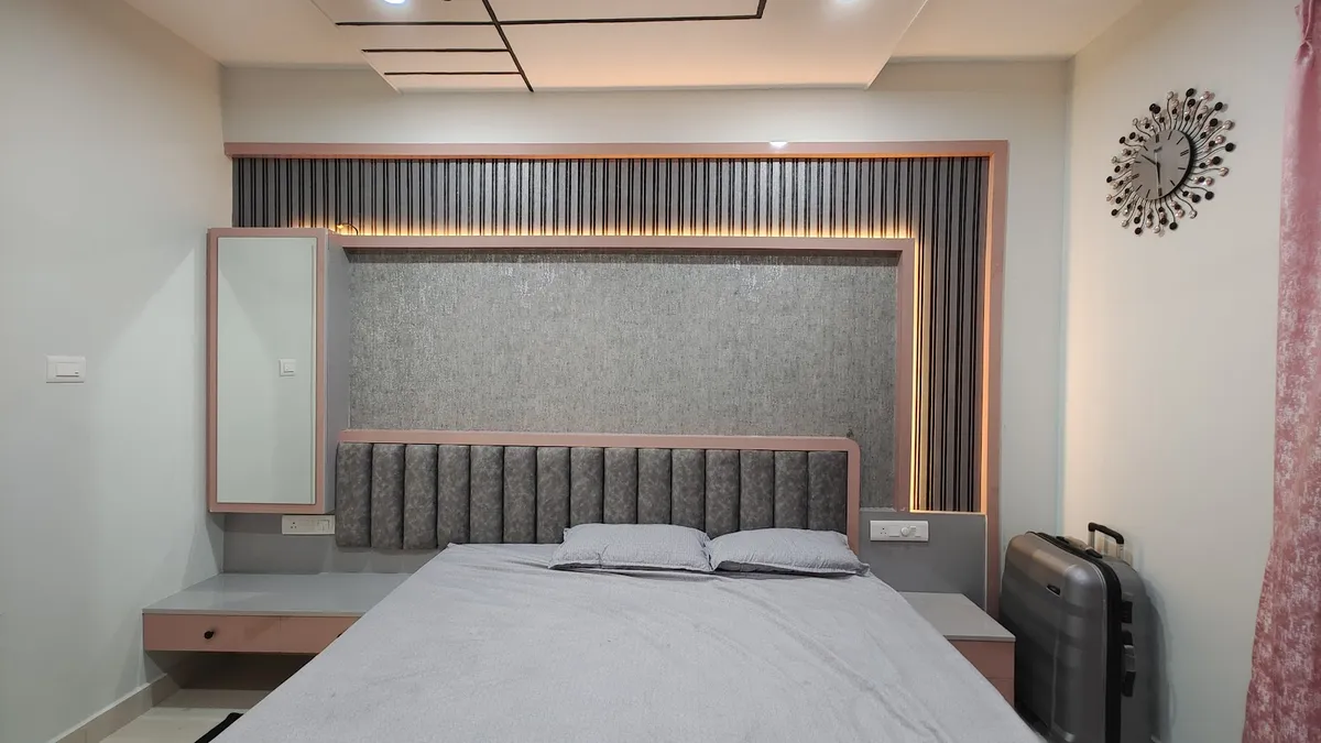 Bedroom with a channel-tufted grey headboard framed in pink trim, a backlit vertical-fluted panel wall, a wall-mounted mirror, and a sunburst wall clock
