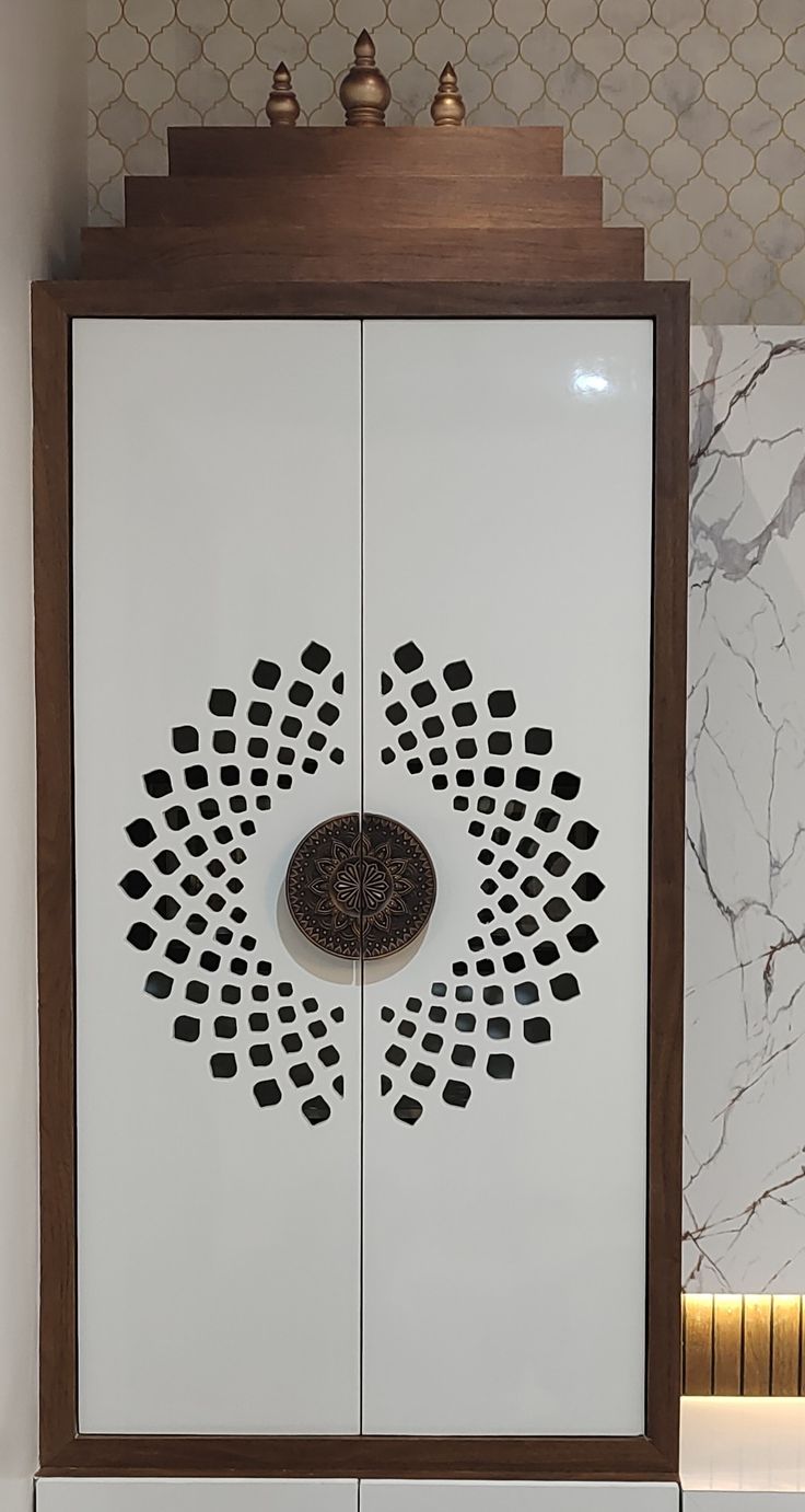 A white lacquered pooja cabinet with a laser-cut mandala jaali pattern and antique copper door pull