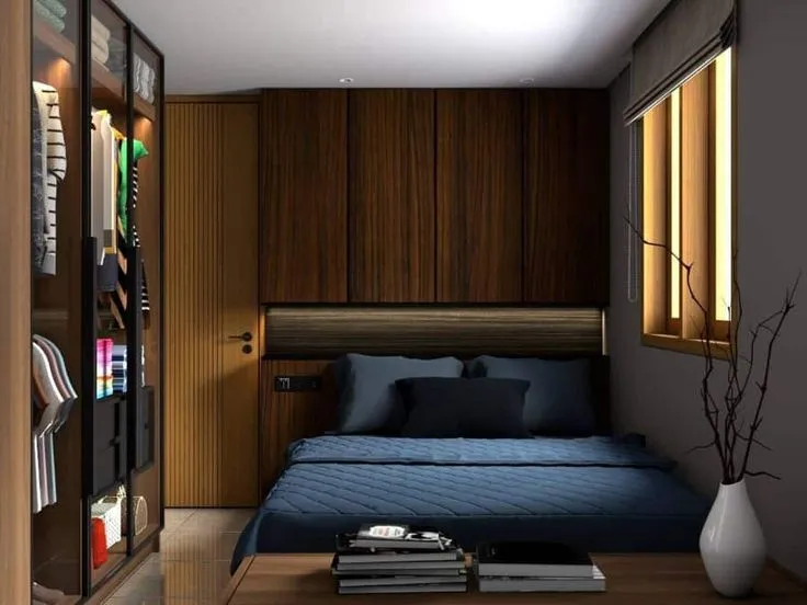 Render of a tight bedroom built almost entirely in dark walnut — a low platform bed in navy linen under an overhead loft storage run with a concealed strip