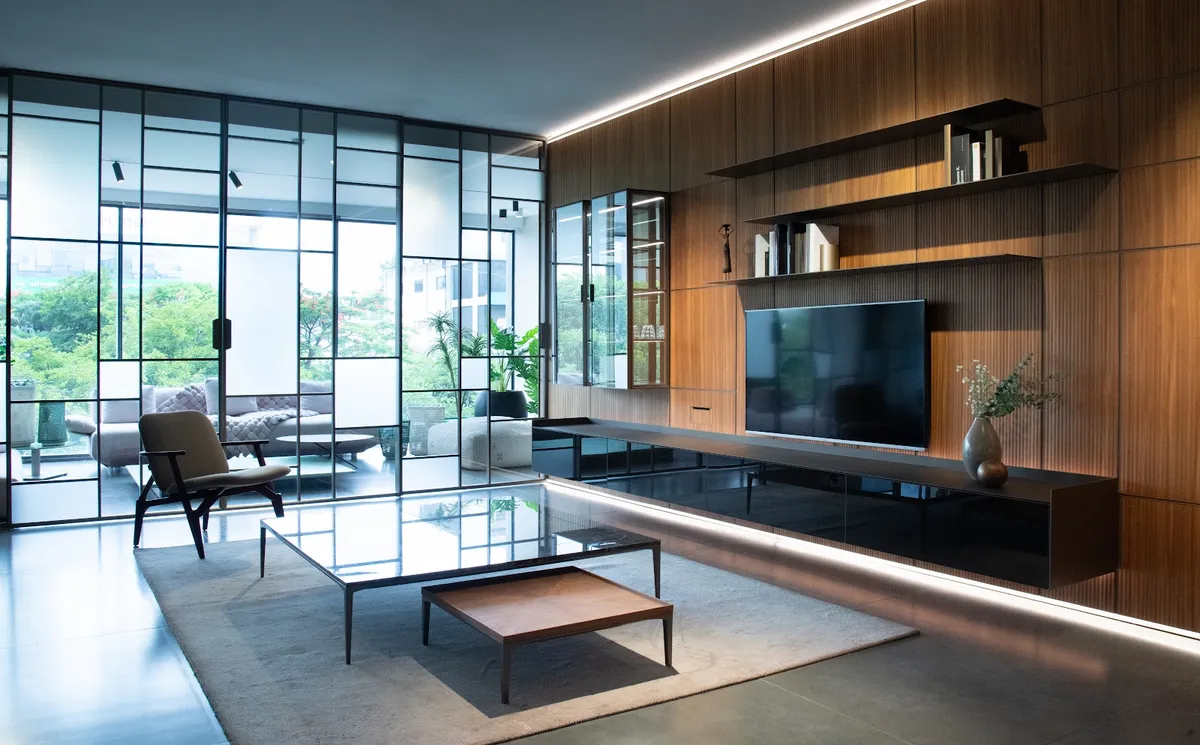 Living room with a full-height steel-framed glass wall opening to a balcony, a backlit fluted-wood TV wall with floating book shelves