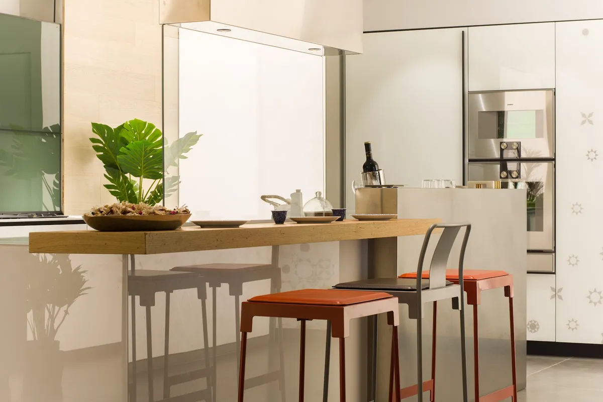 A stainless-steel kitchen island with a built-in oven column, a solid-wood breakfast bar, and orange leather bar stools