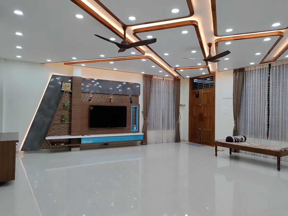 Unfurnished living room under an angular stepped false ceiling ribbed in wood-finish profiles and cove light around two dark fans