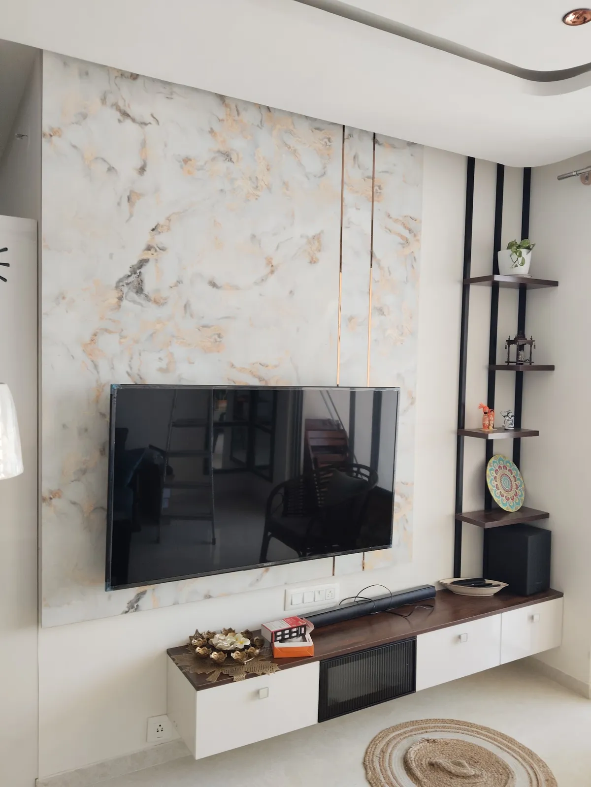 Living room TV wall clad in gold-veined marble with a floating wood-top TV unit below and a black ladder shelf styled with decor in the corner.
