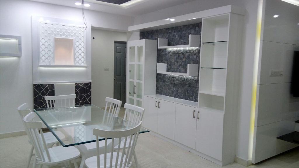 Dining area with a glass-top table seating six, a white crockery display unit with a charcoal mosaic tile backdrop and glass shelving