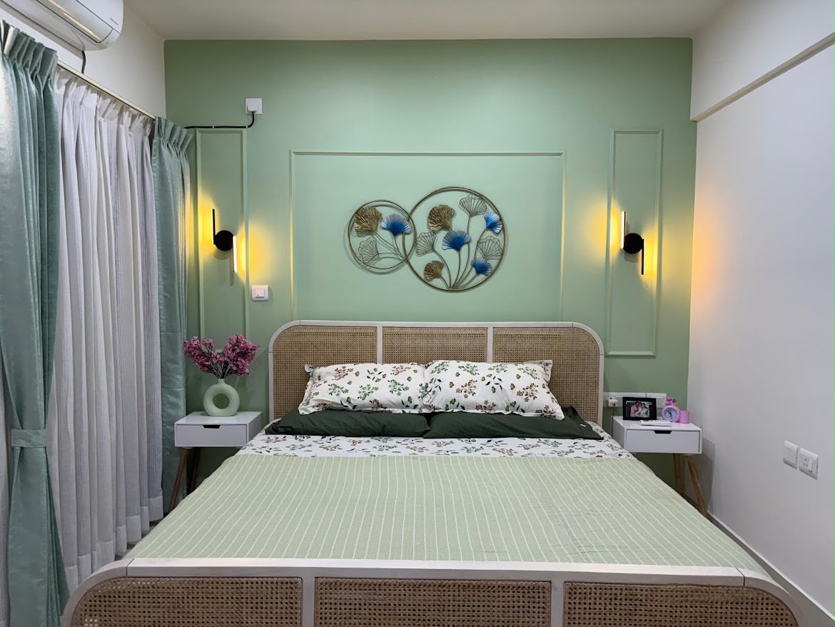 Sage-green bedroom with a rattan cane bed frame, a moulded wall panel holding a two-ring floral metal art piece