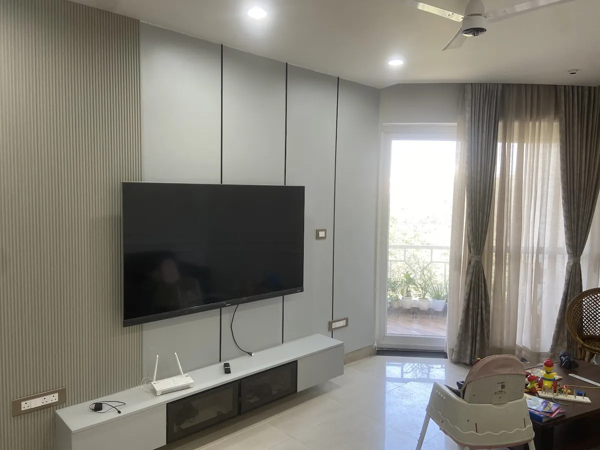 Lived-in living room with a pale grey grooved-and-fluted TV panel wall, a wall-hung white console holding a router