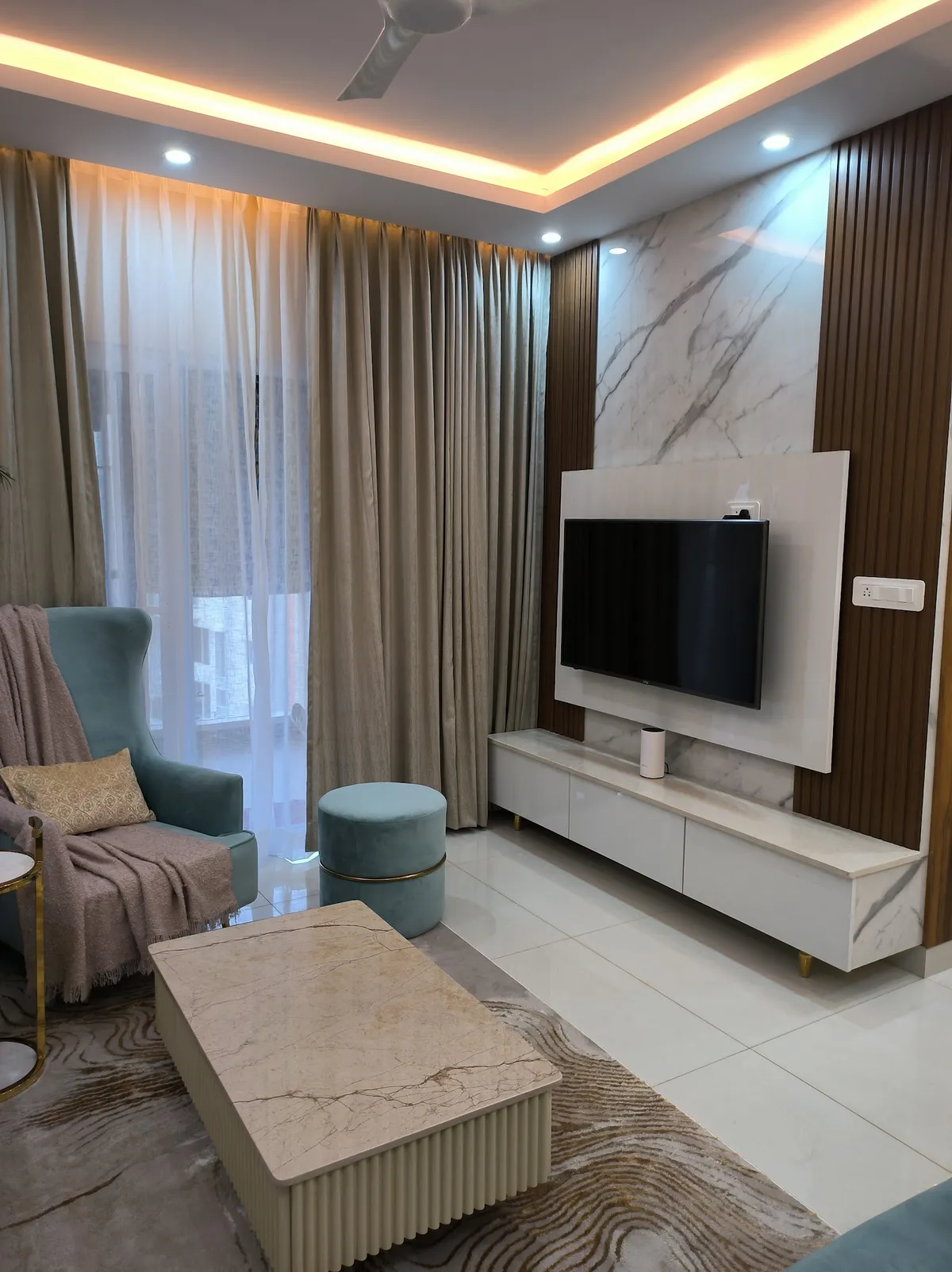 Living room with a white marble TV panel flanked by teak fluted strips, a marble-topped console on slim brass legs