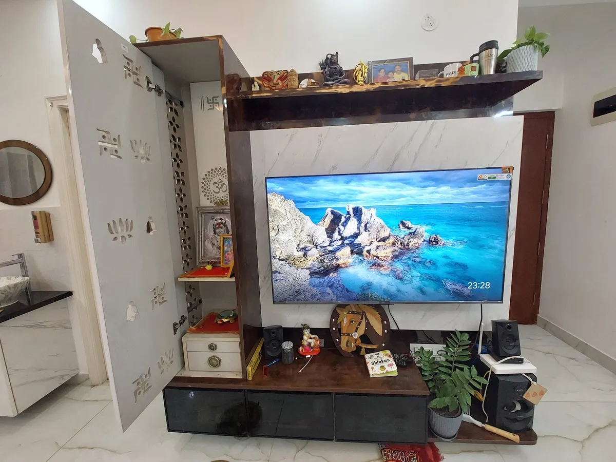 Lived-in living room TV wall in marble-print laminate with a dark wood ledge of brass idols and family photos above it