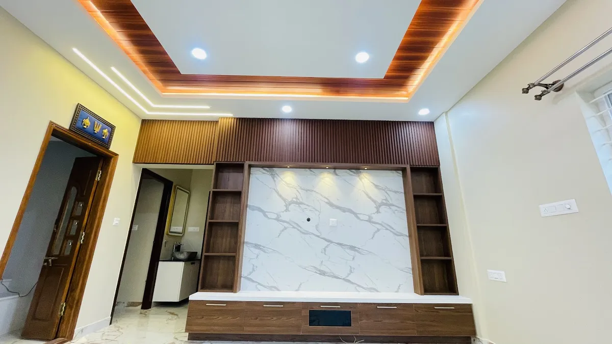 Living room TV feature wall with a book-matched white marble panel framed by dark wood fluted panelling and open shelving, cove-lit wood ceiling drop above