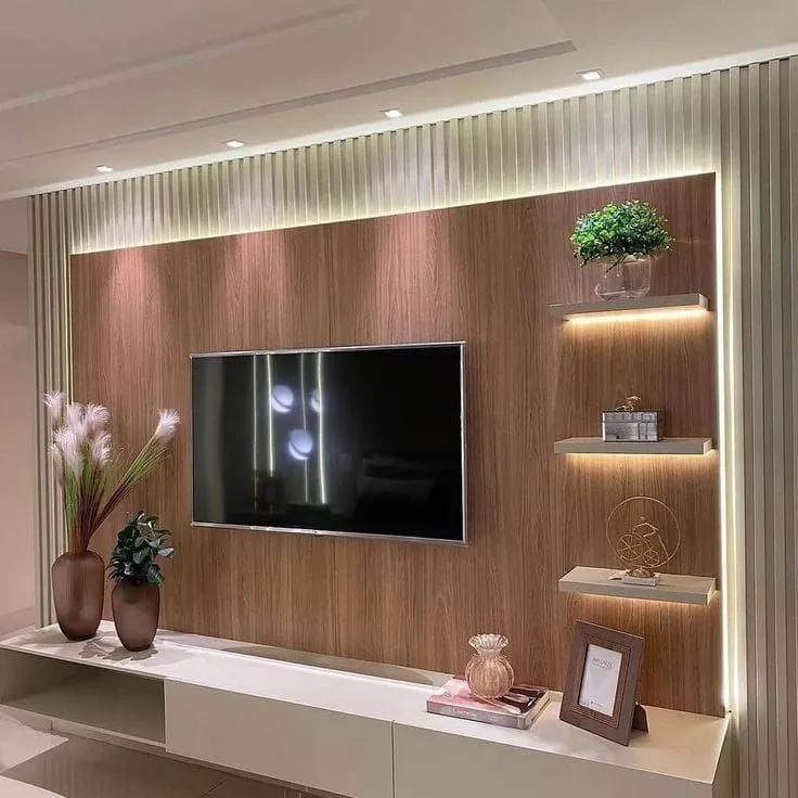 TV unit wall with a walnut veneer panel, backlit floating display shelves styled with plants and decor, and fluted cream side panels under a cove-lit ceiling.