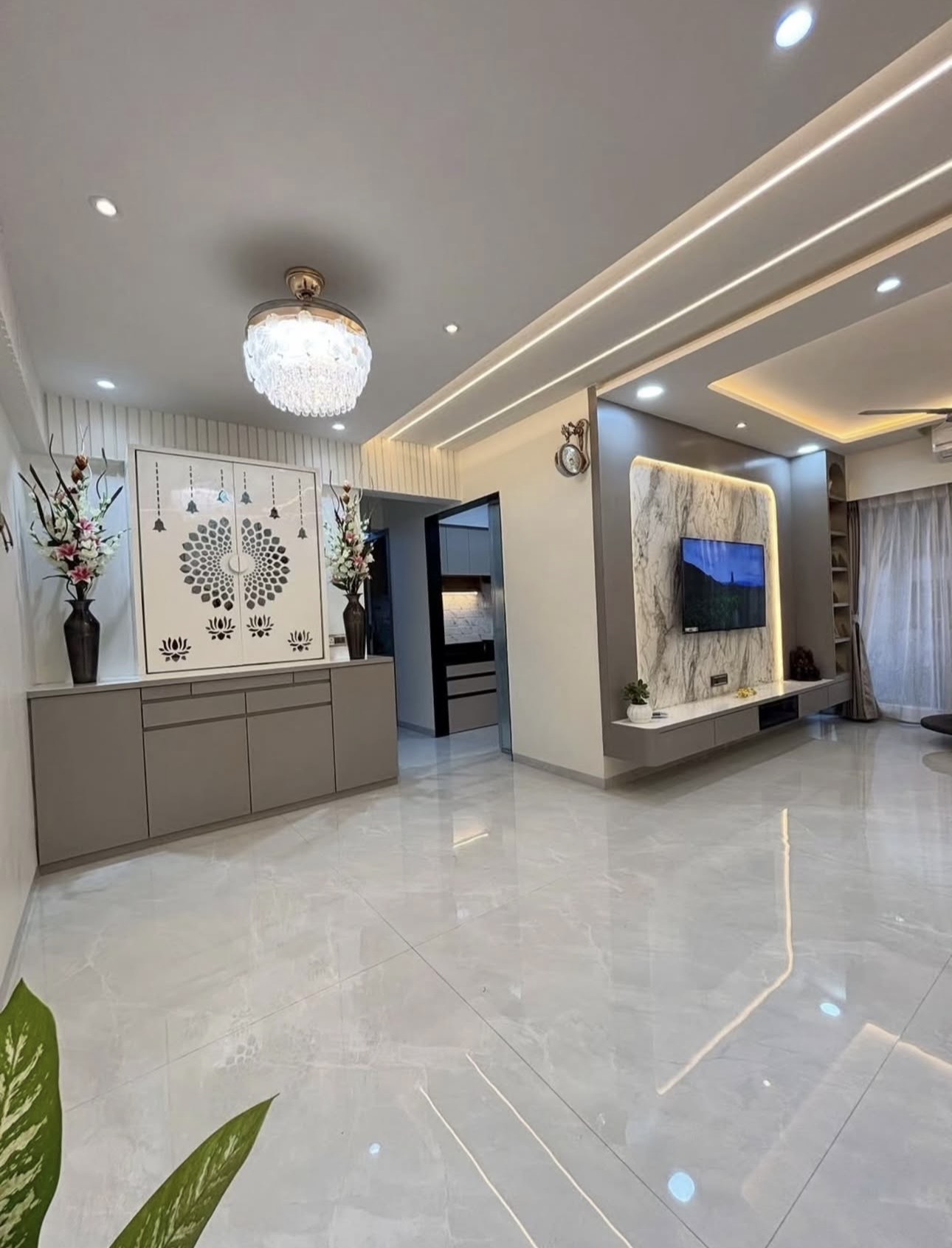 Living room with a marble-clad TV feature wall and floating console, and a taupe cabinet with laser-cut lotus-and-bell jaali doors
