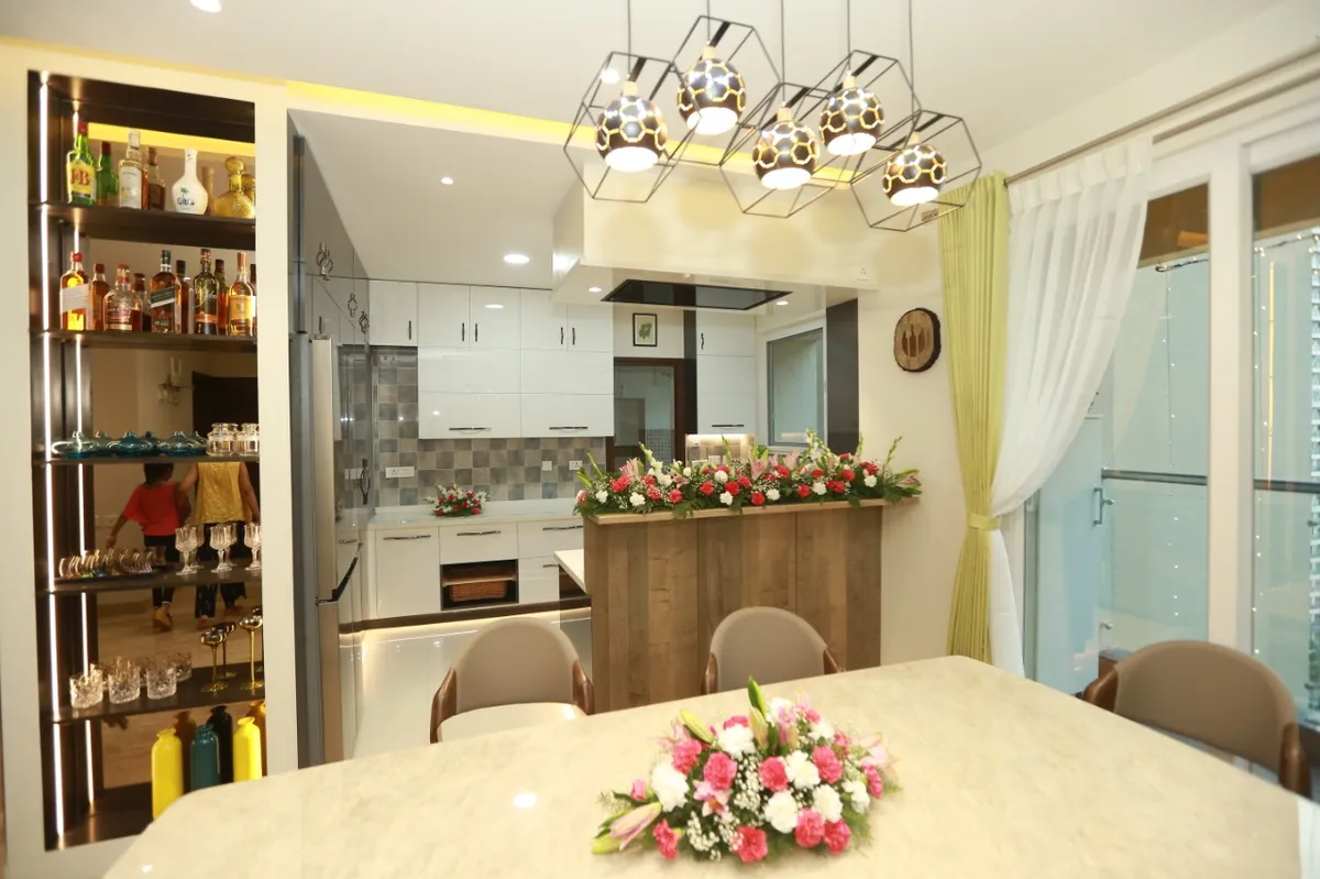 Dining area with a geometric honeycomb pendant light cluster over a marble-top table, a built-in bar display shelf, and an open kitchen beyond.