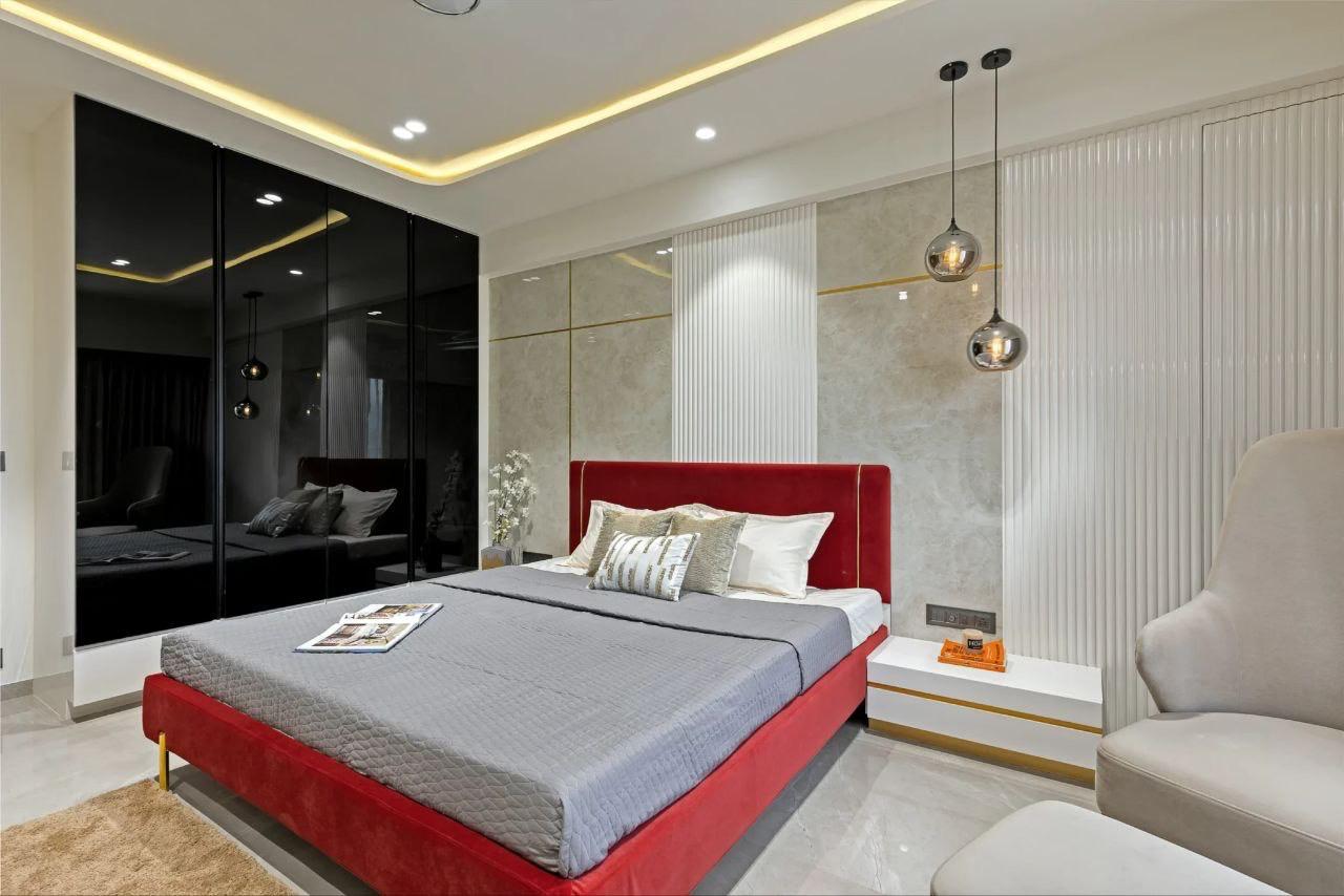 Bedroom with a red velvet upholstered bed, a mirrored black glass wardrobe wall, a fluted stone-textured headboard wall with gold trim