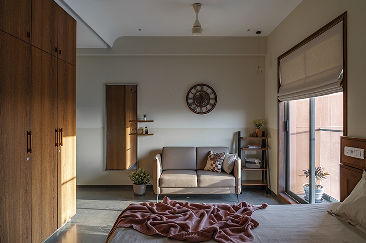 Bedroom with a walnut wardrobe, a small grey loveseat and full-length mirror against a two-tone wall
