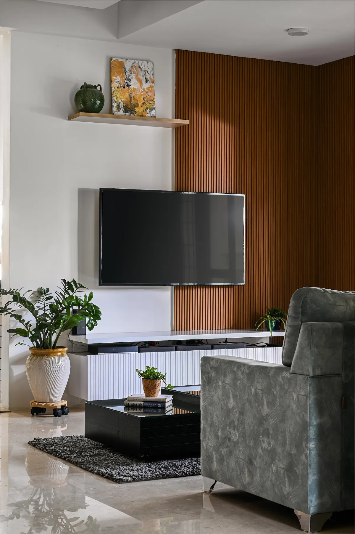 Living room where a wall-mounted TV sits on white plaster beside a full-height teak slat panel, over a white fluted console