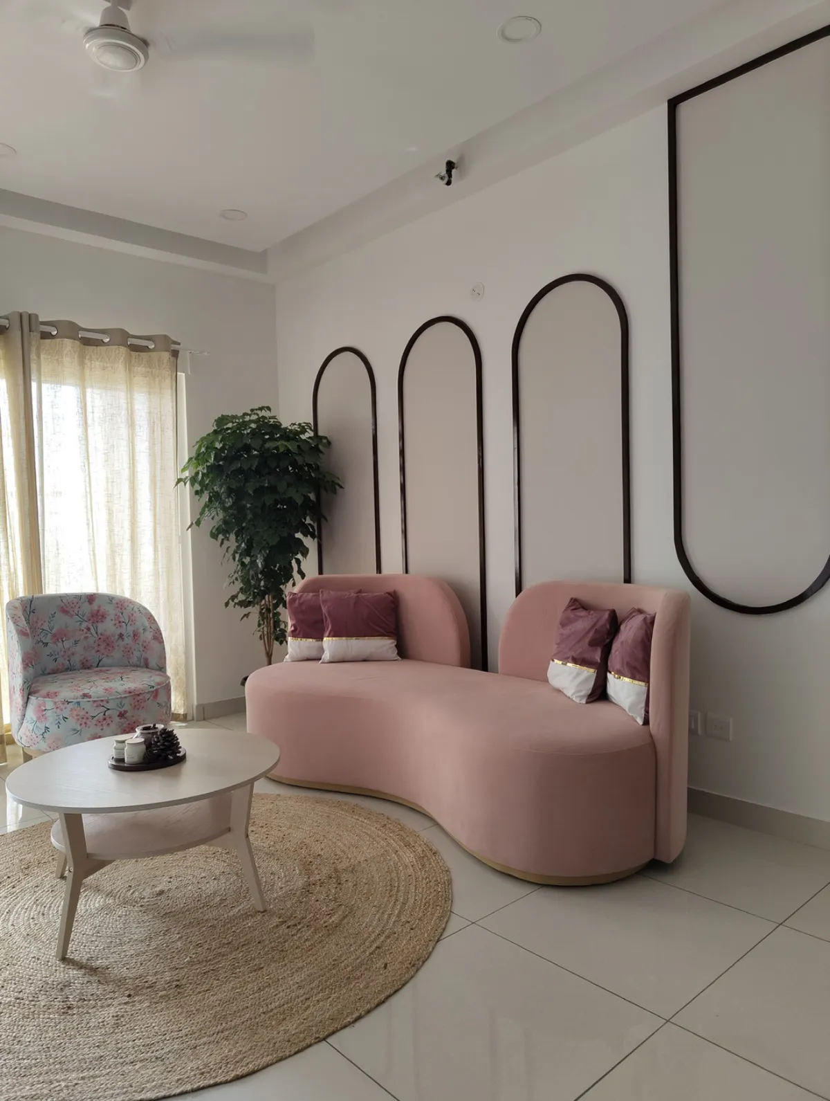 Living corner with a kidney-shaped blush velvet sofa on a brass base, set against three slim black arch mouldings on a white wall