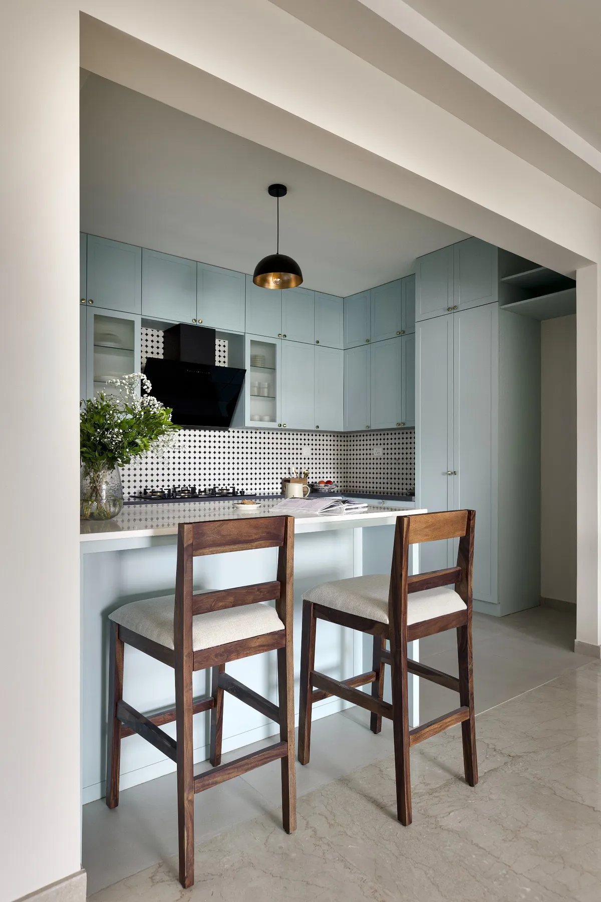 Pastel blue shaker-style kitchen with a black-and-white geometric mosaic backsplash, a black-and-brass dome pendant light over the breakfast counter