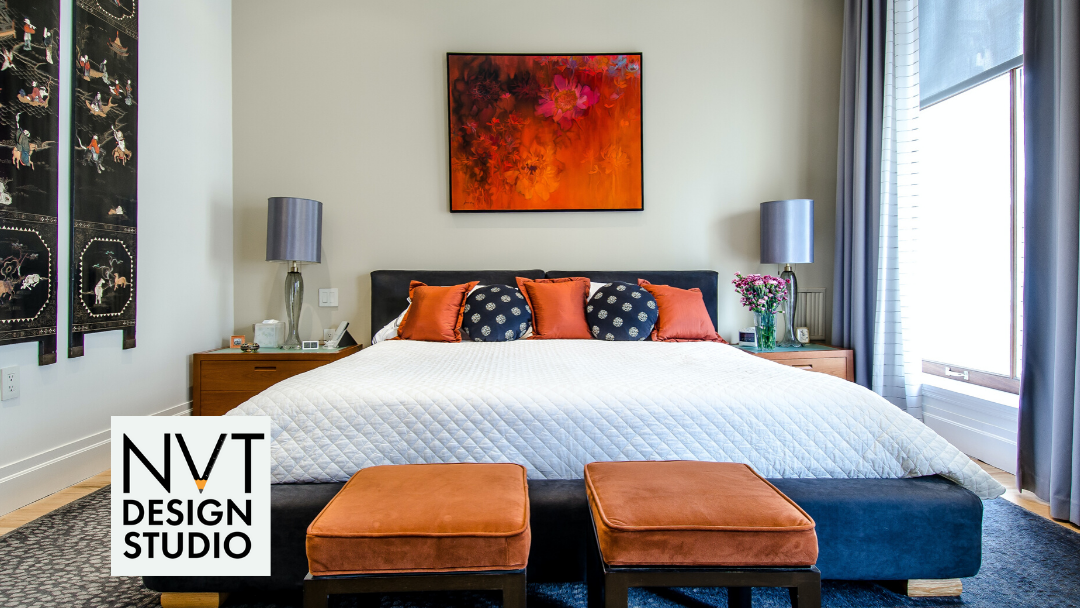 Bedroom with a navy upholstered bed and bench, orange velvet ottomans and cushions, and a large fiery orange abstract painting above the headboard.