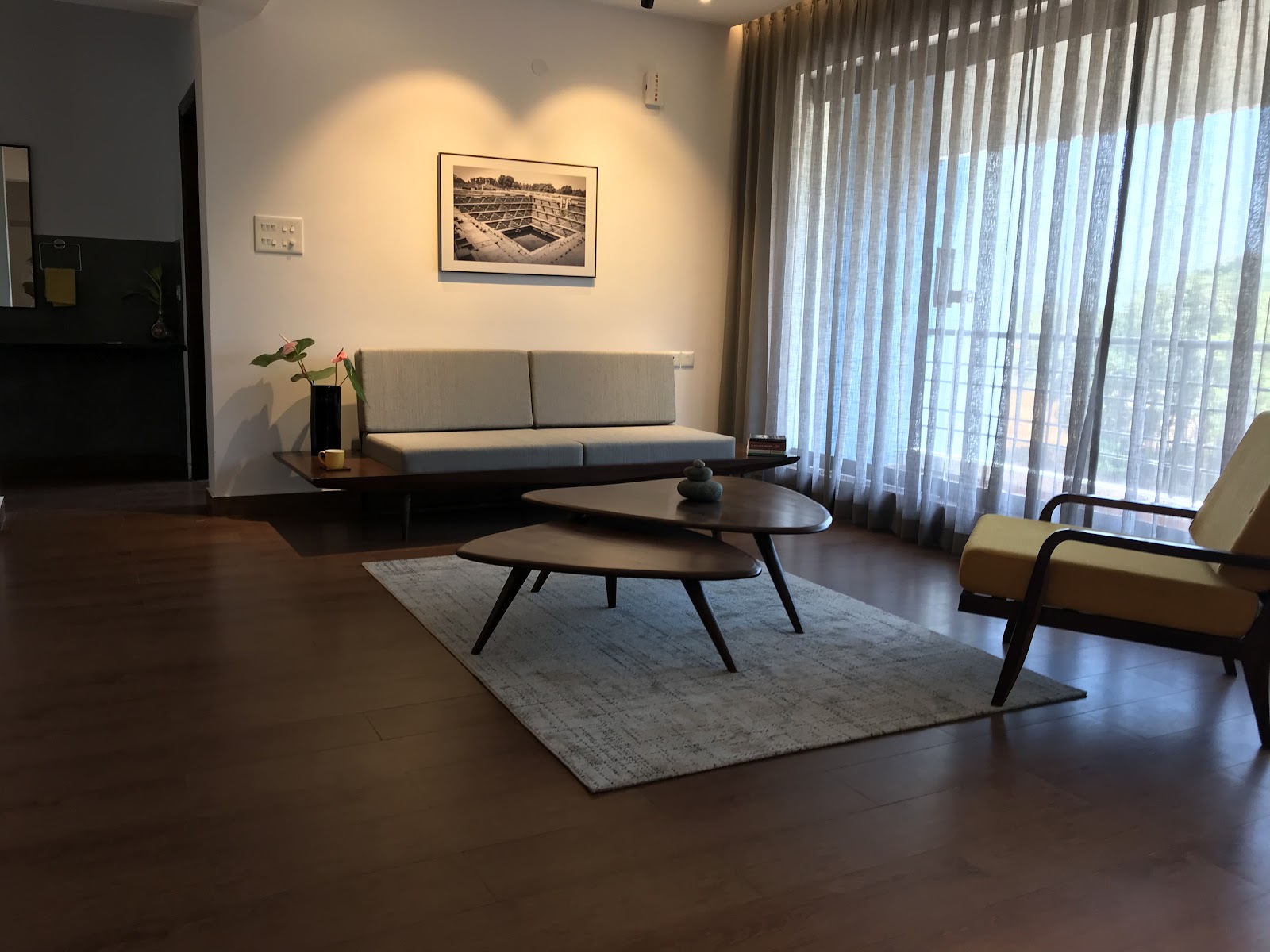 Mid-century living room with a low wood-framed sofa, a mustard-yellow accent armchair, organic-shaped nesting coffee tables on a grey rug
